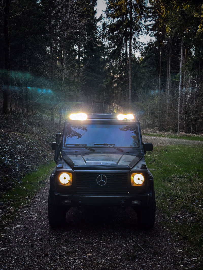 Dark G-Class with Walger Works roof rack in the forest, headlights on